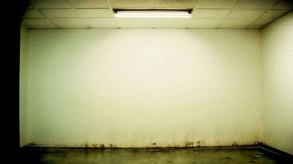 Moody grunge-style room with stained walls and fluorescent ceiling light.