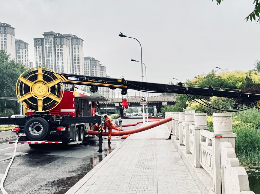 Flood management team operating machinery in urban area for water drainage.
